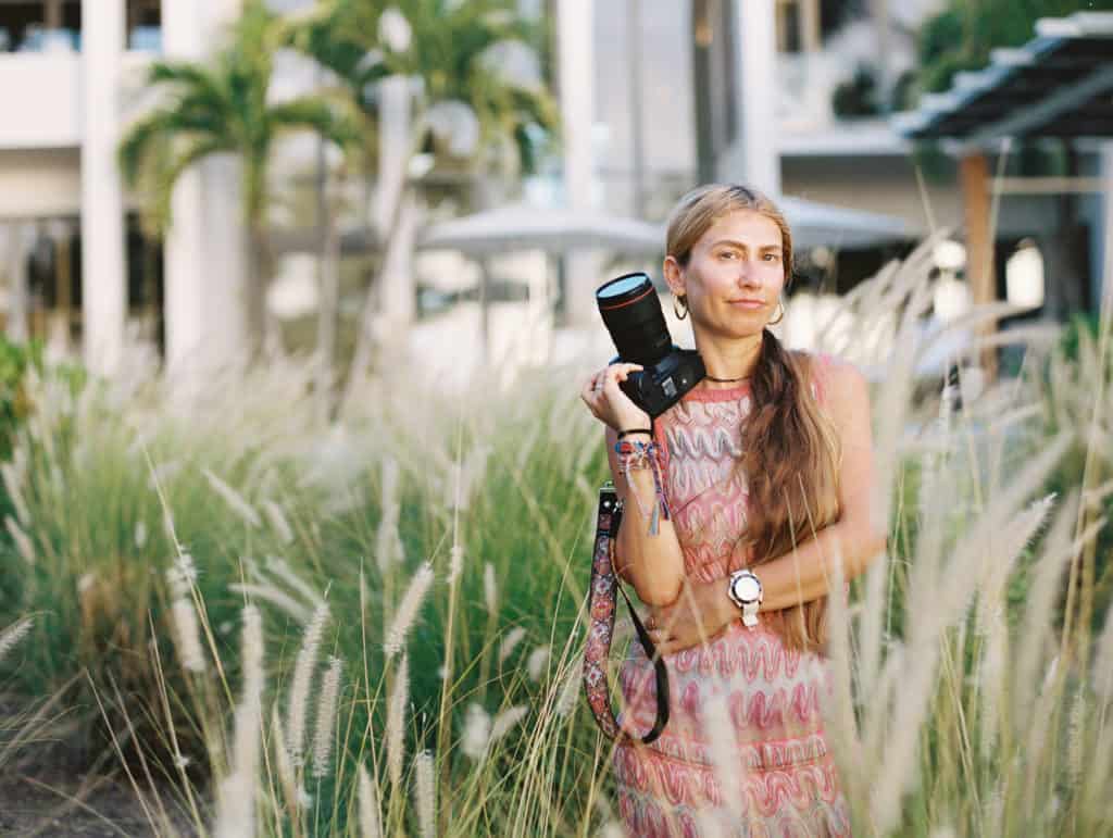 Woman stands in field holding camera while shooting a wedding for clients she booked after using sales funnels for photographers