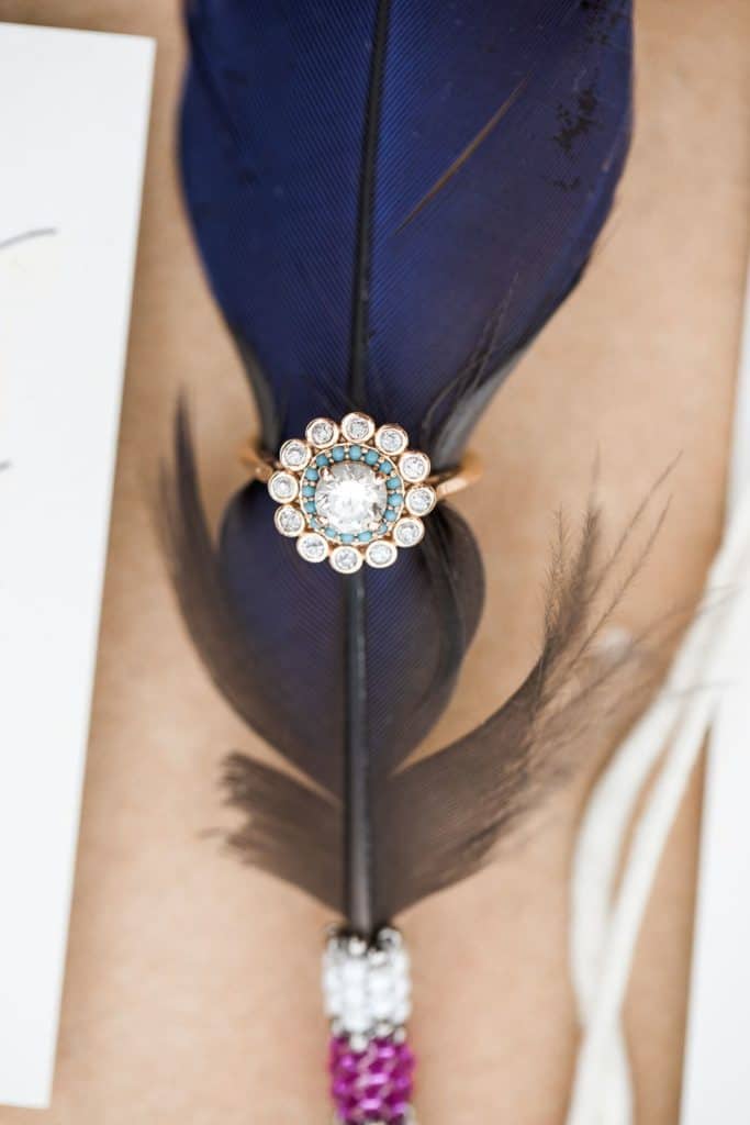 Diamond and turquoise engagement ring uniquely positioned on feather for southwestern-inspired wedding flat lay photography