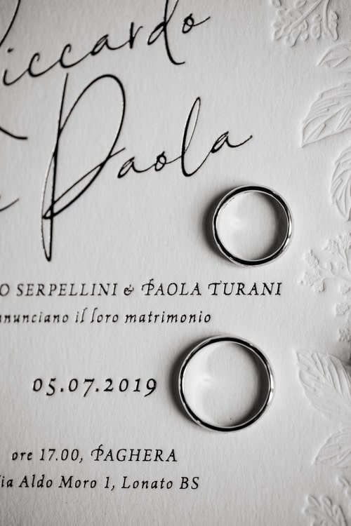 A closeup photograph of wedding rings against an embossed, white wedding invitation